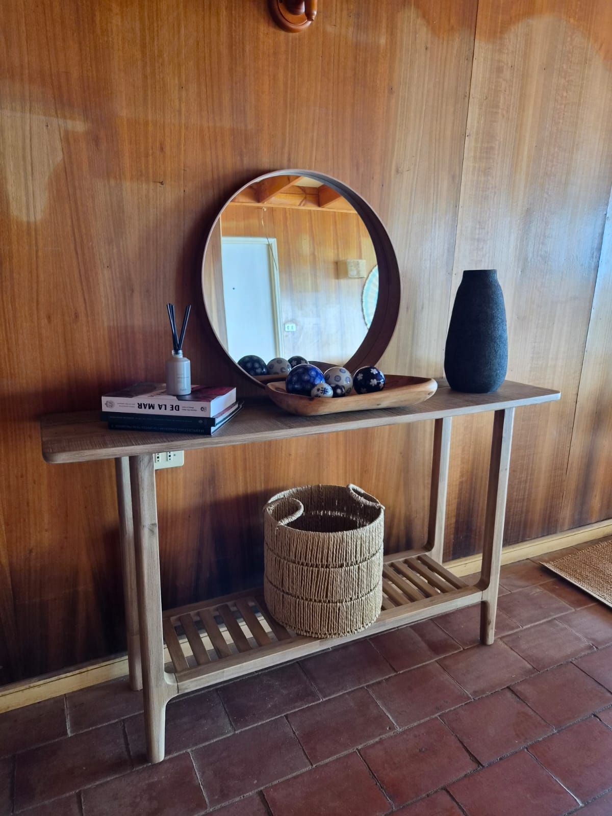 Rincón de la entrada con consola de madera, espejo redondo y canasto de fibra