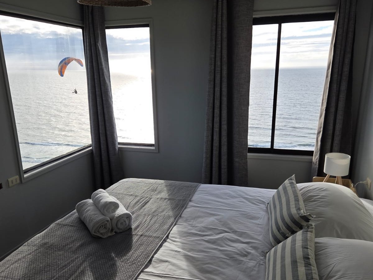 Doble Deluxe: cama king frente a los ventanales en esquina, con un parapente sobre el Pacífico